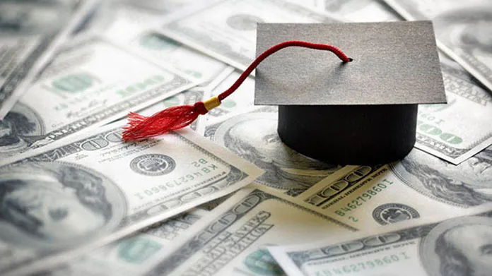 A paper graduation cap sitting on many one hundred dollar bills